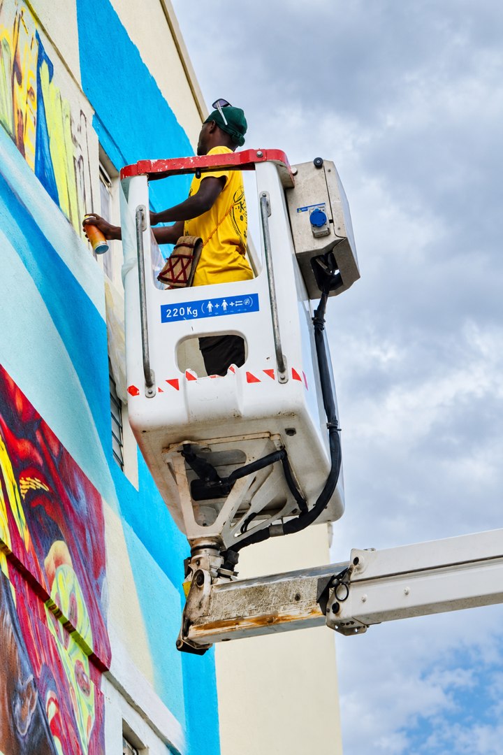 Rayza painting a mural from an aerial lift